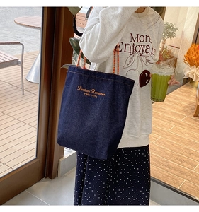 Dettaglio della borsa tote in denim blu con ricamo giallo e spalline sottili rosse