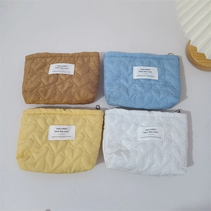 Detailed view of four heart-quilted cosmetic bags in brown, blue, yellow and white