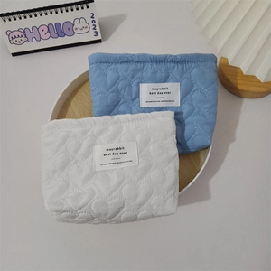 Quilted heart pattern cosmetic bags in light blue and ivory on a wooden tray
