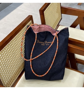 Dettaglio della borsa tote in denim blu con fodera a quadri rossi e ricamo giallo sulla sedia