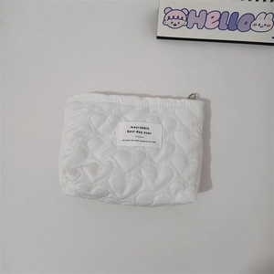 Detail shot of white quilted heart pattern and embroidered label on a compact pouch