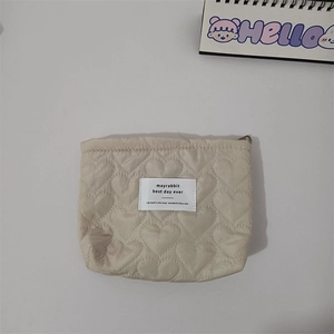 Detail shot of heart quilted beige cosmetic bag featuring a brand woven label on center