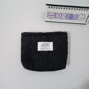 Detail of heart quilted black lipstick pouch with a white woven label and minimalist style