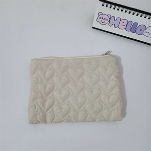 Close-up of heart-shaped quilted pattern and zipper detail on beige mini makeup bag