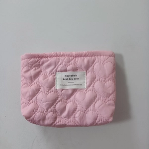 Detail of pink quilted cosmetic bag with heart pattern and woven brand label