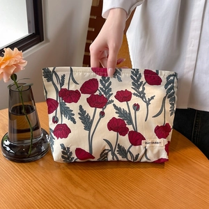 Floral makeup bag with red poppy prints and woven label on a wooden desk setting