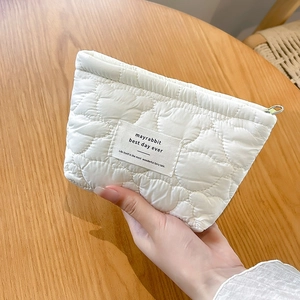 Detailed heart-quilted texture and brand label on white portable cosmetic pouch