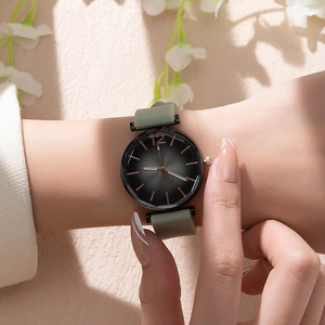 Close-up of a dark green silicone strap quartz watch with golden dial accents on a wrist