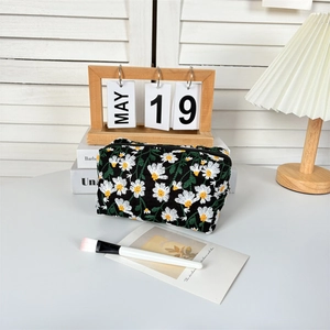 Detailed embroidery of white daisies and green leaves on black canvas cosmetic bag