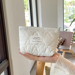 Close-up of white heart-quilted cosmetic bag with brand label held in hand