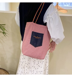 Dettaglio borsa tote in tela a quadri rossi con tasca in denim e tracolla a righe