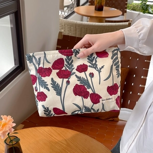 Floral makeup bag with red poppy patterns and zipper closure in a coffee shop setting
