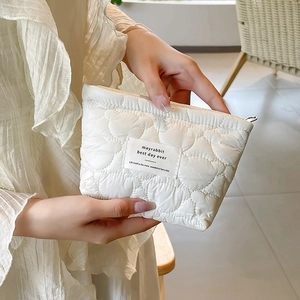 Detail of white quilted cosmetic bag with heart texture and woven label held by hand