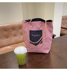 Dettaglio borsa tote in tela a quadri rossi con tasca in denim e ricamo a testo inciso