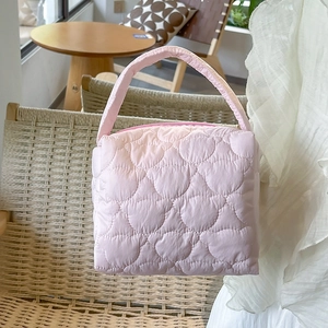 Pink quilted nylon cosmetic bag with top handle placed on a woven rattan chair