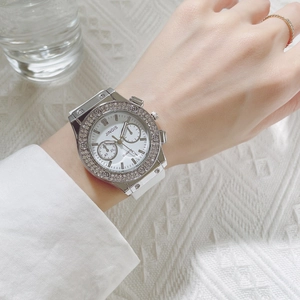 Gros plan d'une montre à quartz pour femme avec lunette sertie de diamants et bracelet blanc