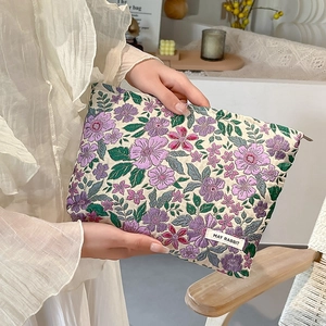 Macro detail of floral jacquard embroidery on a cream travel makeup bag with brand label
