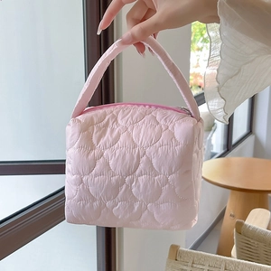 Pink quilted heart-patterned makeup bag held by hand, featuring smooth zipper closure