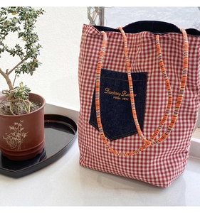 Dettaglio borsa tote a quadretti rossi con tasca in denim e manici in corda intrecciata qui