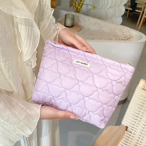 Close-up of lilac quilted cosmetic bag with teddy bear stitching and logo detail