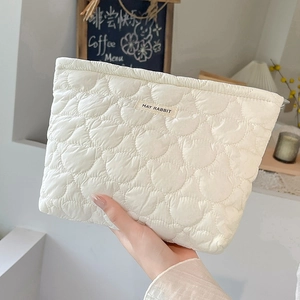 Close-up of quilted cream makeup bag with wavy stitching and MAY RABBIT label
