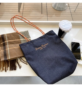 Dettaglio della borsa tote in denim blu con corde intrecciate colorate e ricamo di testo