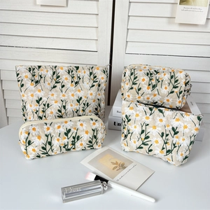 Close-up of embroidered white daisies and green vines on cream canvas makeup bags