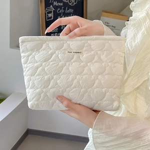 Elegant white quilted makeup bag with heart pattern and woven label held in a cafe setting