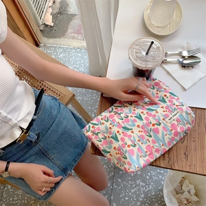Detailed shot of a floral makeup bag with pink tulips and a branded label on a wooden table