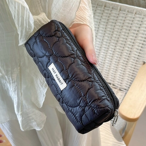 Detail of black heart quilted pencil case with white brand label and soft puffy texture
