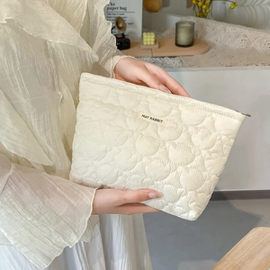 Detail view of cream quilted heart texture and fabric logo label on a cosmetic bag