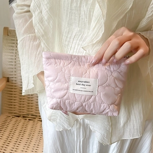 Quilted pink makeup bag with heart stitching and logo tag held by a hand in soft light