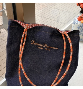 Dettaglio della borsa tote in denim con ricamo arancione e manici in corda colorata