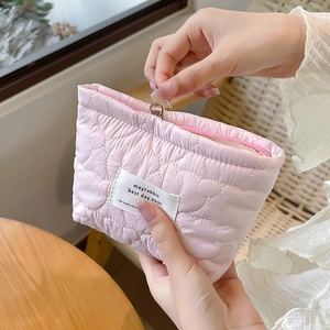 Detailed view of pink heart quilted cosmetic bag with zipper and logo tag being held