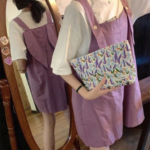 Detail of floral tulip makeup bag held with a purple overall dress in a warm setting