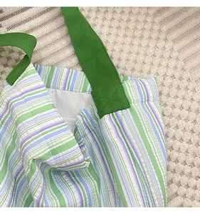 Nahaufnahme der Kreuznaht an einer grün gestreiften Canvas-Tasche mit Faltenstruktur