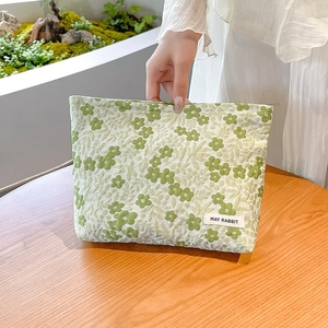Detail of light green floral jacquard makeup bag with May Rabbit label on wooden table