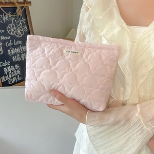 Pink heart quilted travel makeup bag with brand label held in hand for cosmetic storage