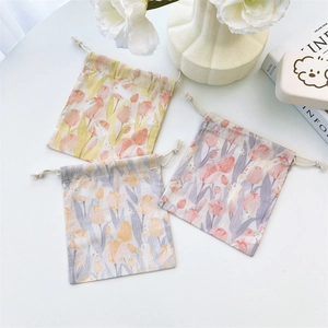 Three canvas drawstring pouches with tulip prints arranged on marble with greenery