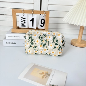 Detailed embroidery of white daisies on a beige fabric cosmetic storage bag