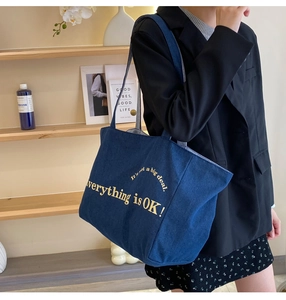 Große blaue Denim-Stofftasche mit gelber Aufschrift an der Schulter des Models