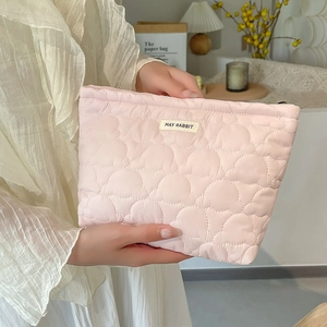 Pink quilted cosmetic bag with heart-shaped stitching and brand label held by a hand