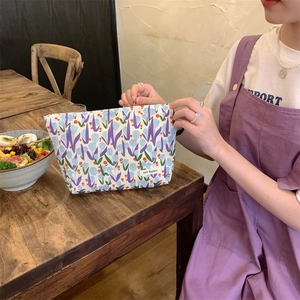 Close-up of a floral makeup bag with purple tulips held by a hand in a warm indoor setting