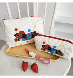 Detail of white quilted cosmetic bags with cute puppy embroidery and red zipper
