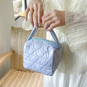 Detail of light blue heart-quilted cosmetic bag with sturdy handle and zipper