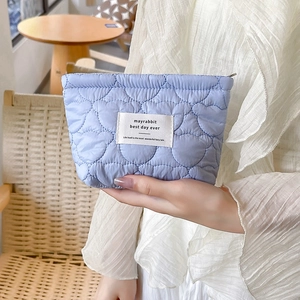 Detail of light blue quilted makeup bag with heart stitching and woven label patch