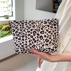 Close-up of leopard print corduroy makeup bag held by hand in a cozy cafe setting