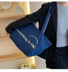 Detail der dunkelblauen Denim-Tragetasche mit gelbem Slogan-Print und breitem Trageriemen