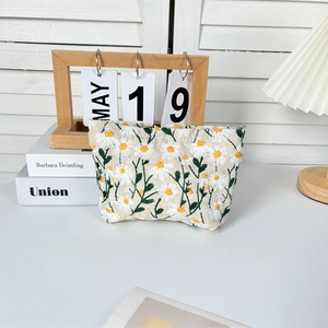 Detailed embroidery of white daisies and green leaves on a beige canvas travel makeup bag