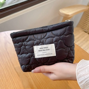 Detailed view of black quilted heart pattern fabric and branded woven label on the pouch